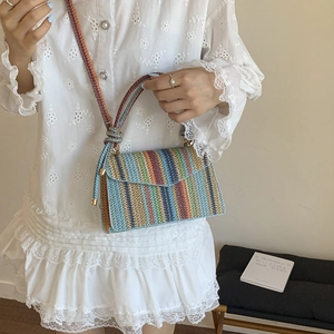 Colorful vertical striped woven straw crossbody bag with textured strap on a white dress