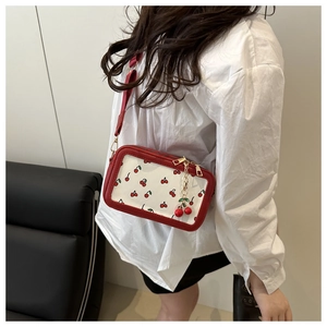 Detail of red cherry print crossbody bag with wide strap and metallic cherry charm