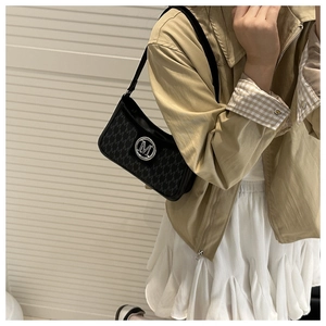 Close-up of black monogram underarm bag featuring a metallic M-shaped round emblem