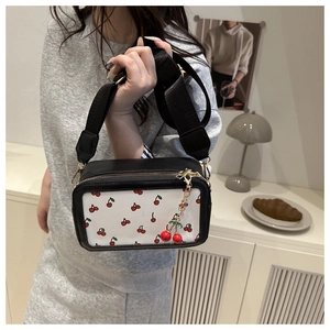 Detail of a black square crossbody bag with cherry prints and a wide fabric strap