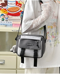 Detail of grey and white crossbody bag with buckle closure and plush doll pendant