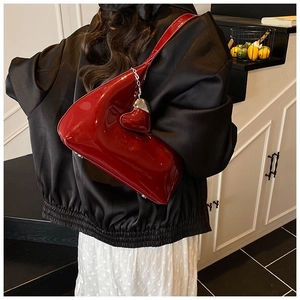 Detail of burgundy patent leather baguette bag with heart charm and slim shoulder strap