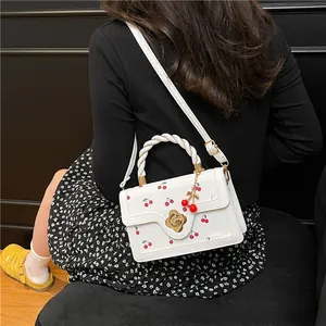 Detail of white cherry print handbag featuring a woven handle and gold flower clasp