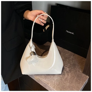 Detail of white patent leather baguette bag featuring embossed logo and heart-shaped charm