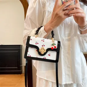 White cherry print crossbody bag with black braided handle and golden flower lock