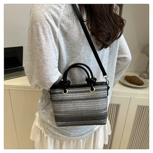 Détail du sac seau tissé avec bordure en cuir noir et finitions métalliques dorées
