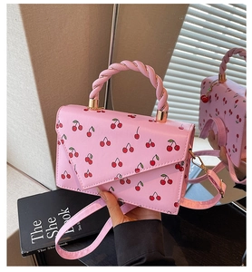 Detalle del bolso rosa con estampado de cerezas, asa trenzada y herrajes dorados