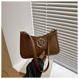 Macro detail of brown shoulder bag showing repeating letter patterns and round metal logo