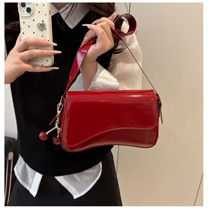 Detail view of glossy red patent leather underarm bag with a cute cherry charm accessory