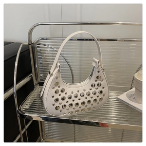 Detail shot of white crescent shoulder bag featuring stylish silver metal rivets on a shelf