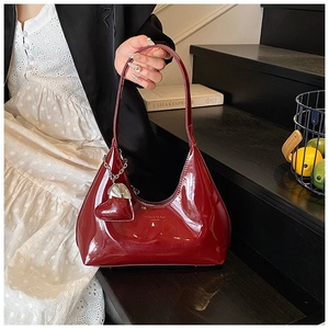Close-up of burgundy patent leather hobo bag featuring a silver chain and heart pendant