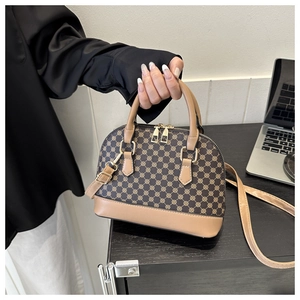 Detail of a brown shell-shaped handbag with geometric patterns and golden metal zippers