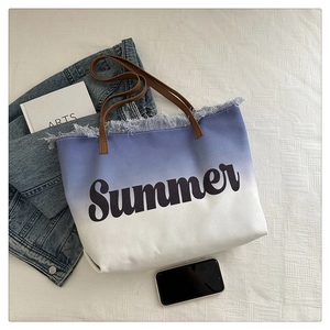 Flat lay of gradient blue tote bag with frayed edges and leather handles on a white surface