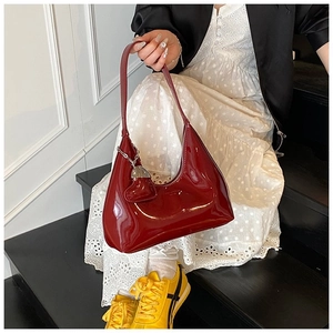 Detail of red patent leather baguette bag featuring a metallic heart pendant on the strap