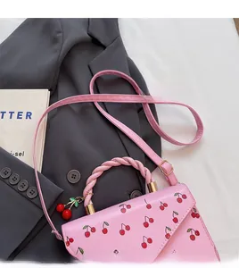 Pink cherry print crossbody bag with woven handle and cherry charm on grey blazer