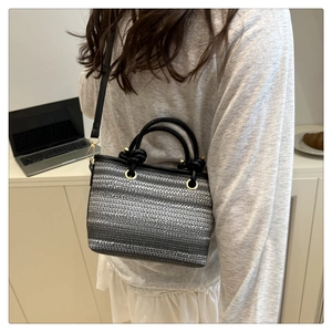 Détail d'un sac seau tissé avec rayures dégradées gris argenté et anses noires en cuir