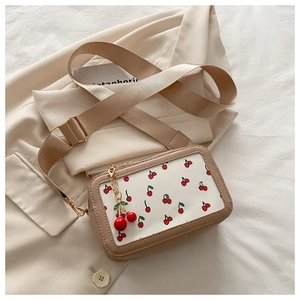 Detail of beige camera bag with cherry print, wide strap and cute cherry charm