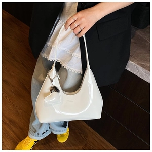 Close-up of white glossy patent leather hobo bag with heart charm and chain detail