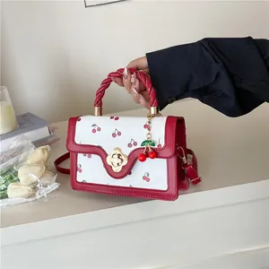 Detail of cherry print handbag featuring a red twisted handle and floral gold buckle
