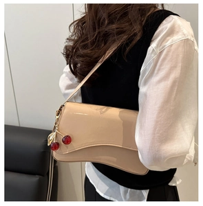 Detail of glossy beige patent leather underarm bag with a decorative cherry pendant
