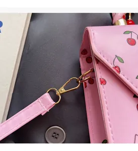 Detail of gold metal hook buckle and pink cherry print on synthetic leather handbag