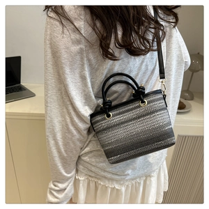 Détail du sac seau en paille tressée avec poignée nouée noire et anneaux métalliques