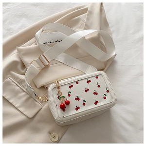 Close-up of white crossbody bag with red cherry print and wide textile shoulder strap