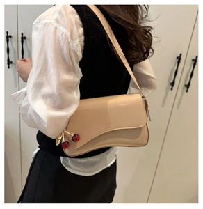Close-up of beige patent leather shoulder bag with cherry charm worn by a model