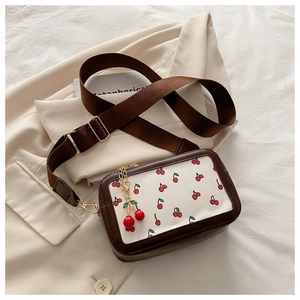 Detail of a square cherry print bag with a wide strap and cherry pendant on soft fabric