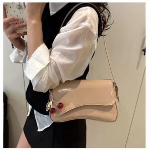 Detail of beige patent leather shoulder bag with cherry pendant and curved flap design