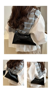 Detail view of glossy black faux leather hobo bag with sleek curved shoulder strap