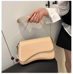 Detail view of beige patent leather shoulder bag featuring a unique wavy flap and cherry charm