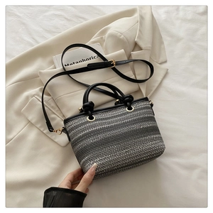 Détail du sac seau en paille tressée avec motif tricolore et bandoulières en cuir noir