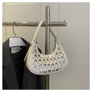 Detail of white crescent bag with silver metallic rivets hanging on a metal rack