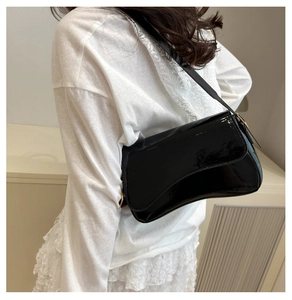 Close-up of black patent leather shoulder bag with gold hardware on female model