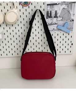 Detail of red minimalist messenger bag on a white pegboard with an adjustable strap