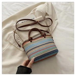 Détail d'un sac seau en paille tissée colorée avec poignées en cuir marron et boucles or