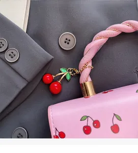 Detail of pink leather handbag featuring cherry patterns and braided rope handle design