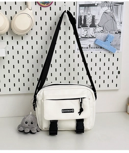 Close-up of white canvas messenger bag featuring black buckles and octopus plush pendant