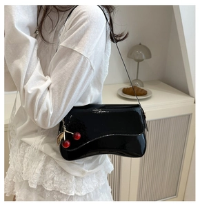 Detail of black patent leather underarm bag with wave flap and cherry metal charm