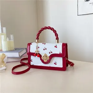 Detail of cherry print mini bag featuring a twisted handle and gold flower clasp