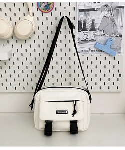 Detail of white canvas crossbody bag with black buckles and adjustable strap on pegboard