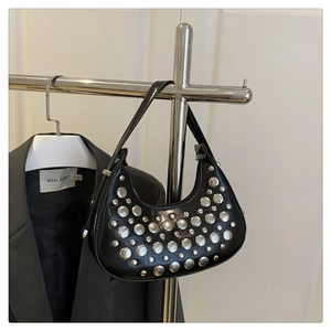 Detail of black crescent hobo bag with silver punk rivets on a polished surface