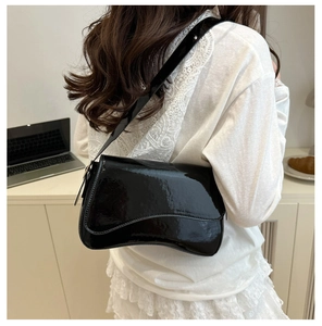 Glossy black patent leather shoulder bag shown on shoulder in a modern indoor setting