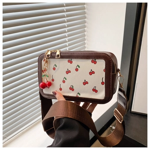 Detail of canvas square bag with cherry print, brown leather trim and 3D cherry charm