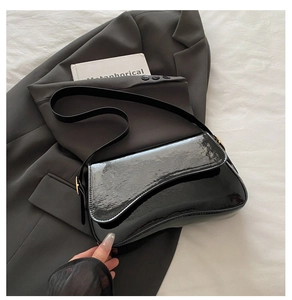 Detail of glossy black patent leather shoulder bag with gold metallic buckle