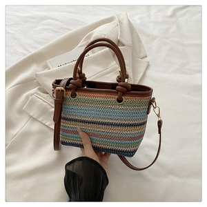 Détail de la texture en paille tressée colorée et des anses en cuir brun sur le sac seau