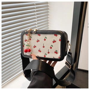 Detail of black crossbody bag featuring a cherry print panel and a decorative cherry charm