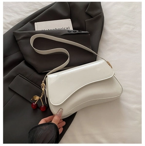 Detail of white patent leather shoulder bag with cherry charm and asymmetric saddle flap