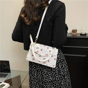White crossbody bag with red cherry pattern and knotted handle on a modern background